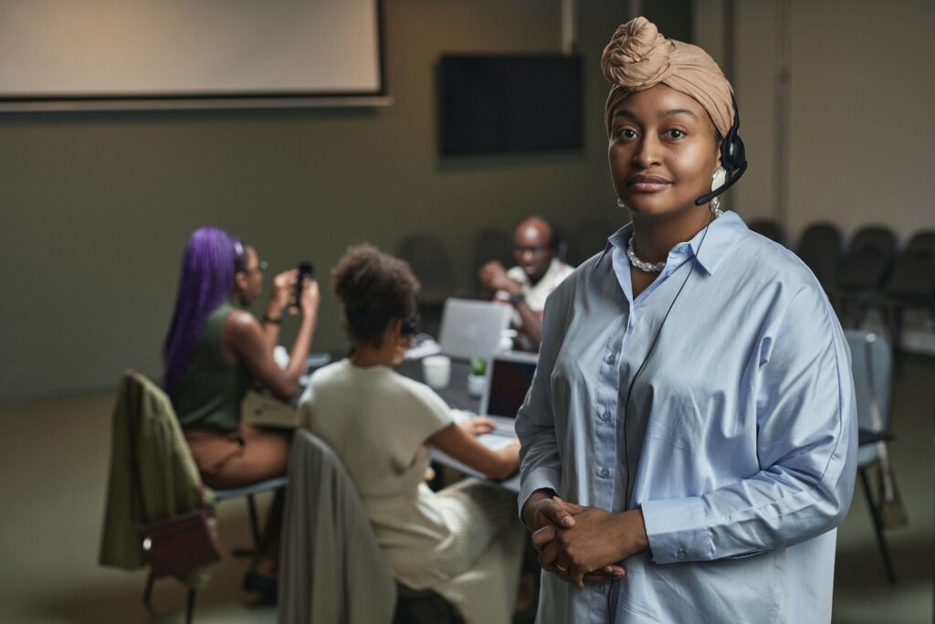 Une conseillère souriante, casque sur la tête, debout à côté d'un groupe de collègues au travail